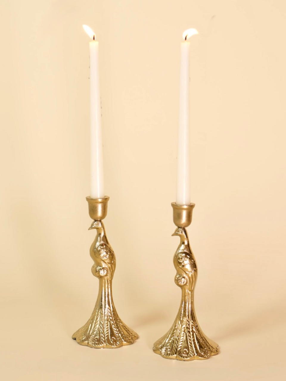 Two gold candle holders with white candles on a beige background
