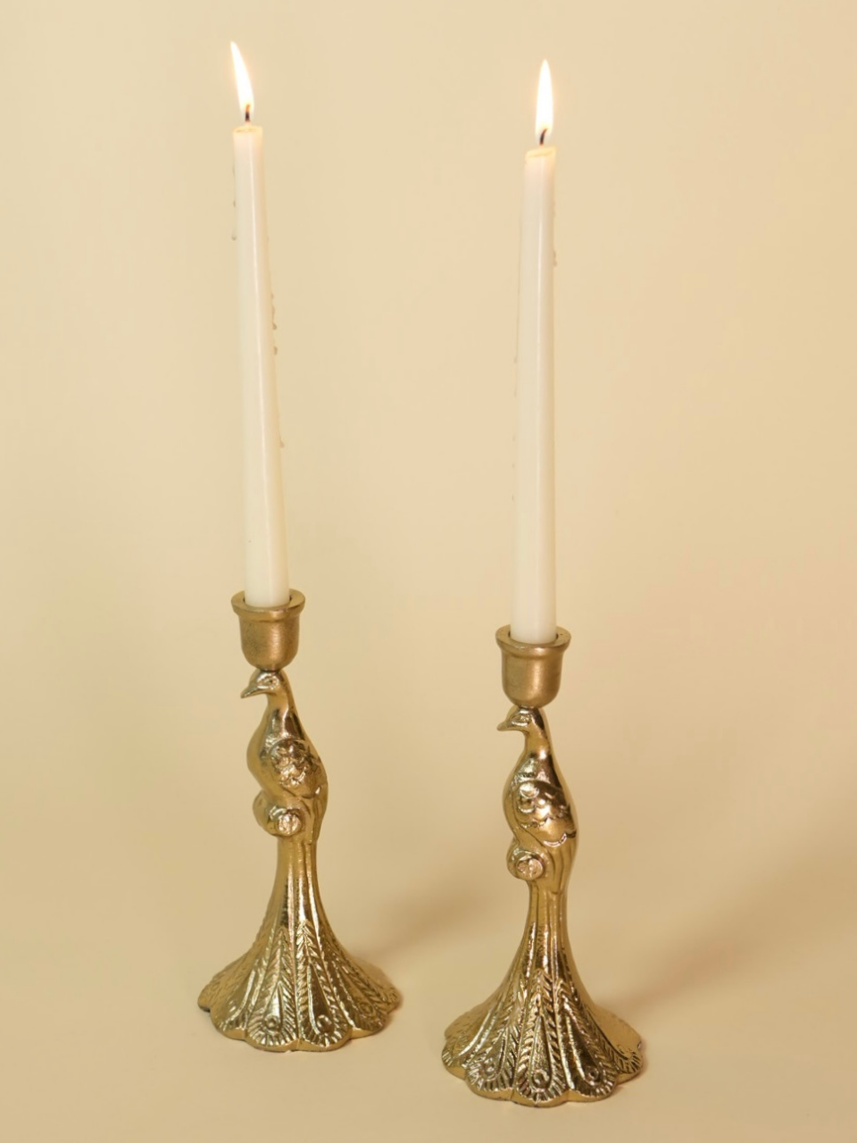 Pair of ornate gold candle holders with lit candles on a beige background