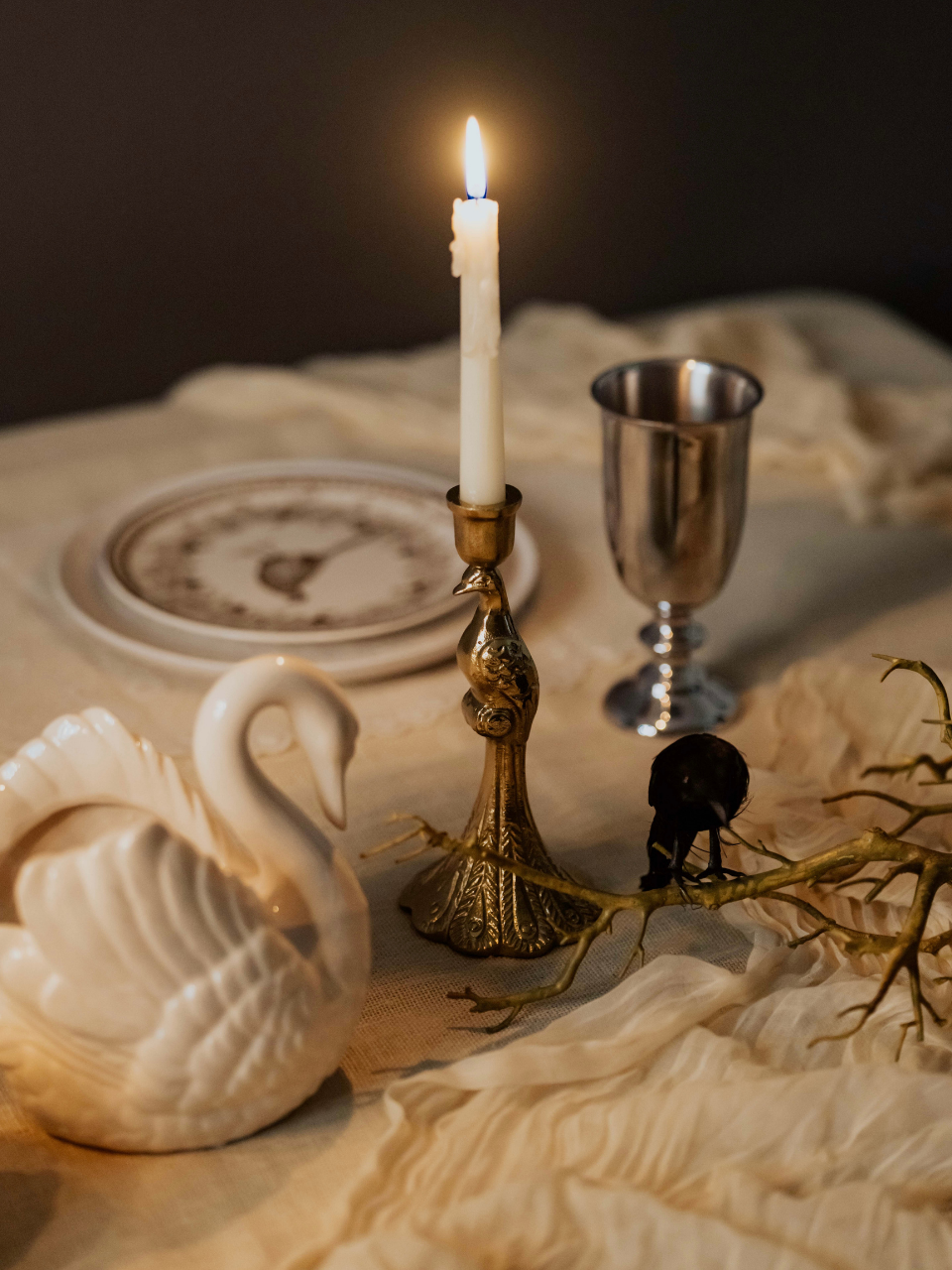 Candlelit table setting with a swan figurine, candlestick, and goblet on a textured surface.