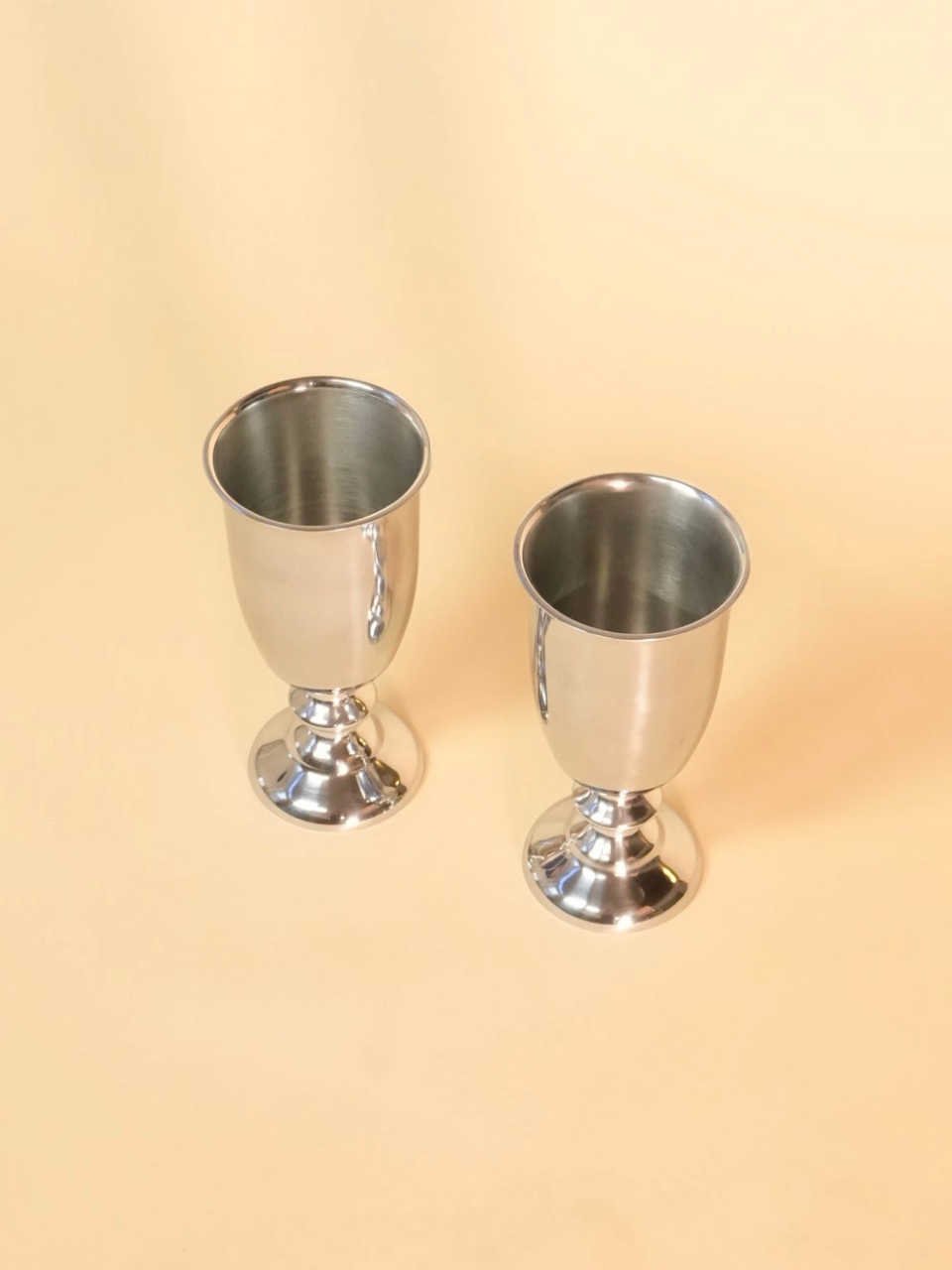 Two silver goblets on a beige background