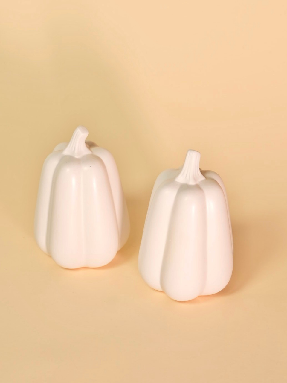 Two white ceramic pumpkins on a beige background