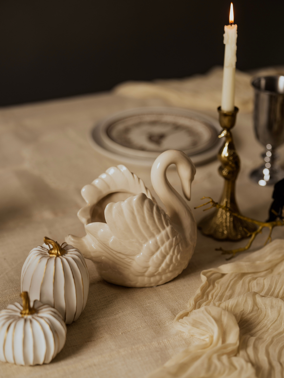 Decorative swan figurine on a table with pumpkins and a candle.