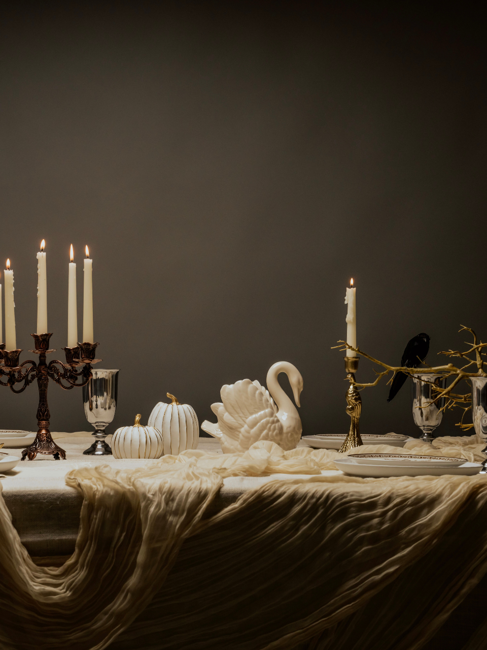Decorative table setting with candles, swan sculpture, and pumpkins against a dark background
