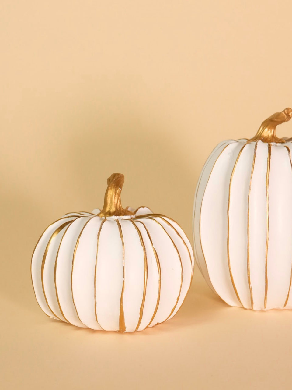 Two white pumpkins with gold accents on a beige background