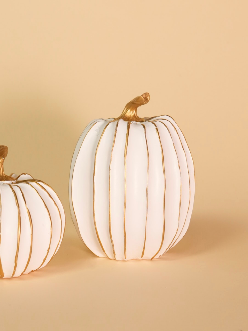 Two white pumpkins with gold accents on a beige background