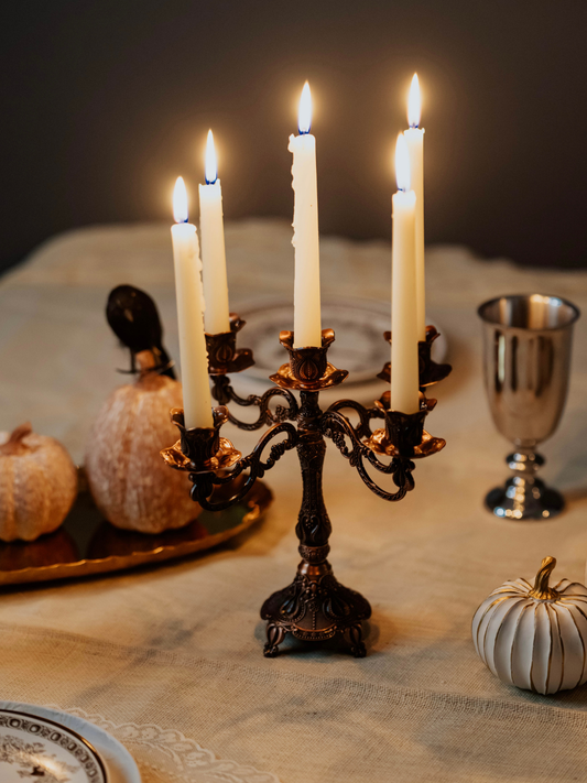 Candlelit candelabrum on a table with pumpkins and goblets in the background