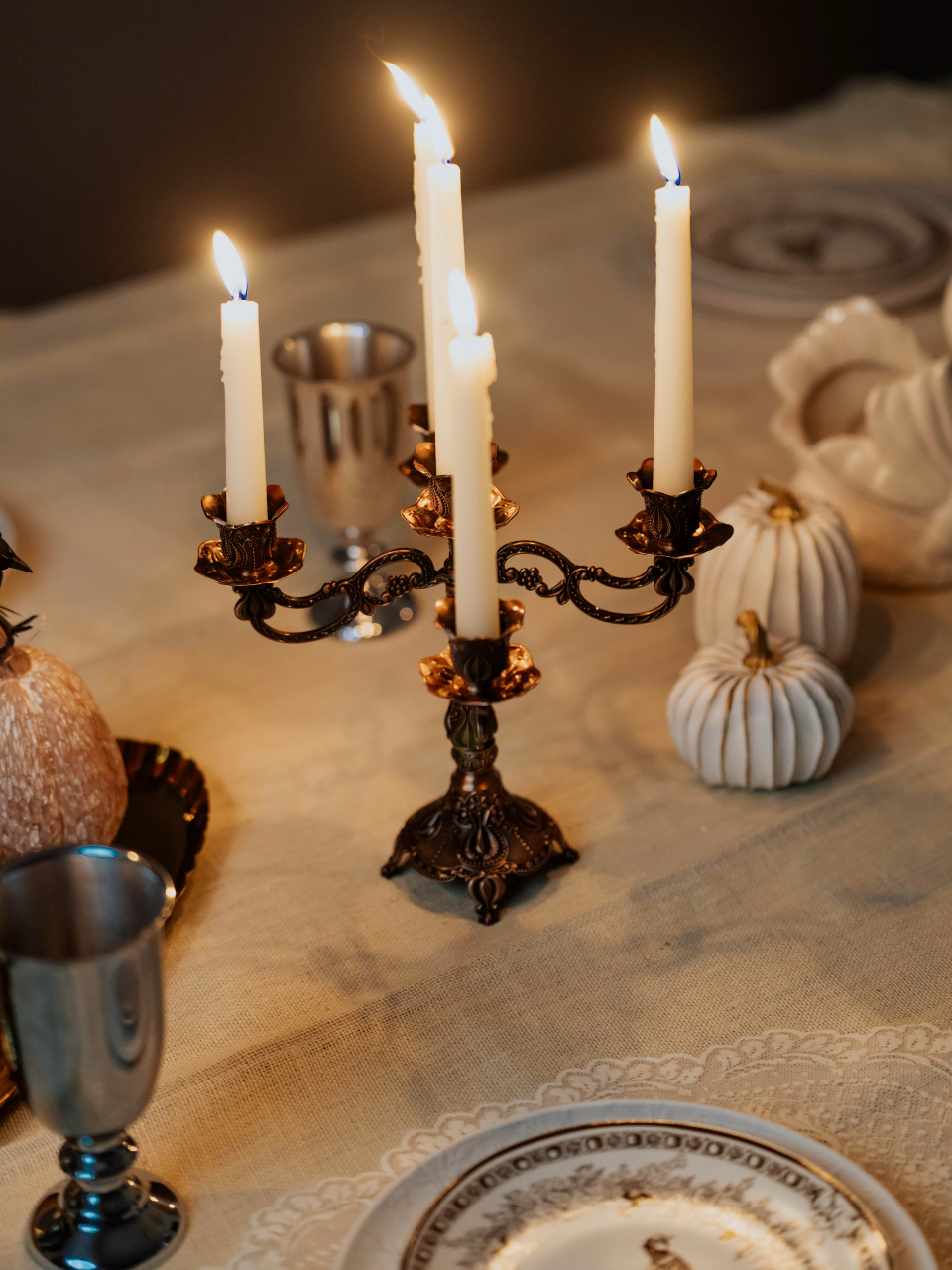 Decorative candelabra with lit candles on a table setting with pumpkins and silver goblets.