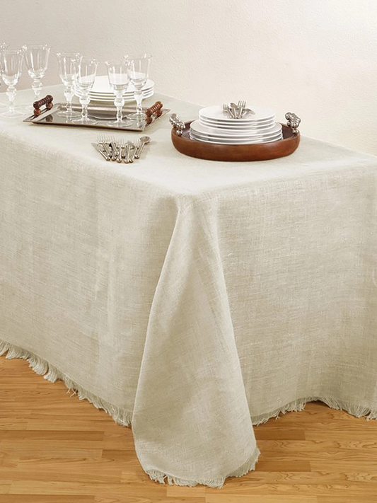 Beige tablecloth on a wooden table with dinnerware and glasses.