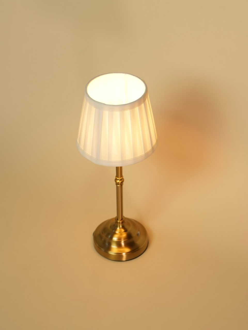 Small lamp with a white shade and brass base on a beige background