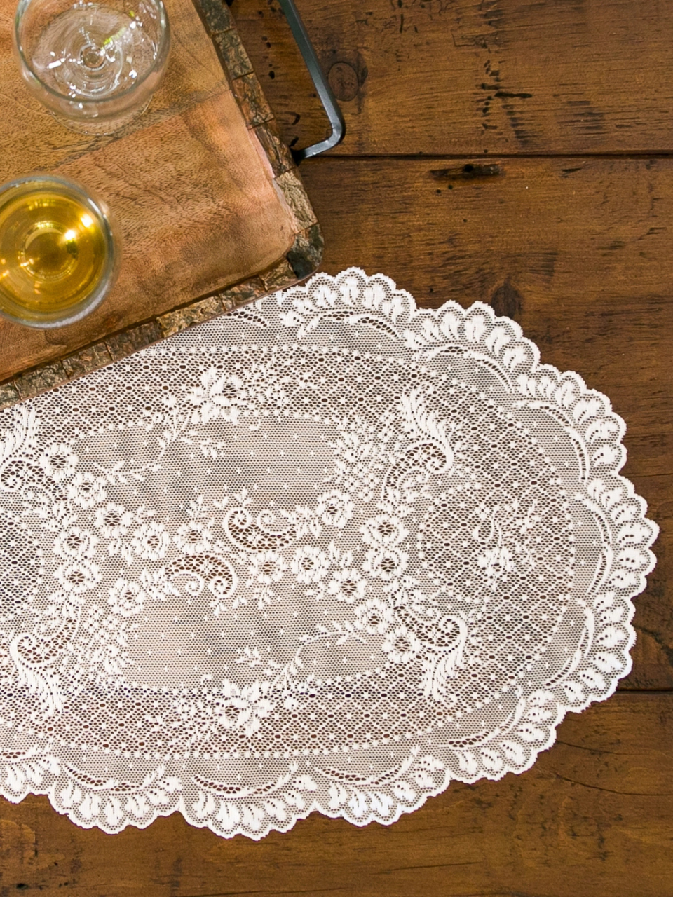 Lace doily on a wooden table with glasses of wine.