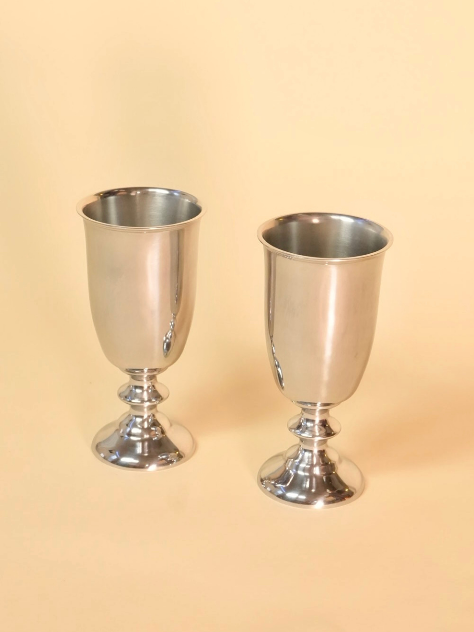 Two silver goblets on a beige background