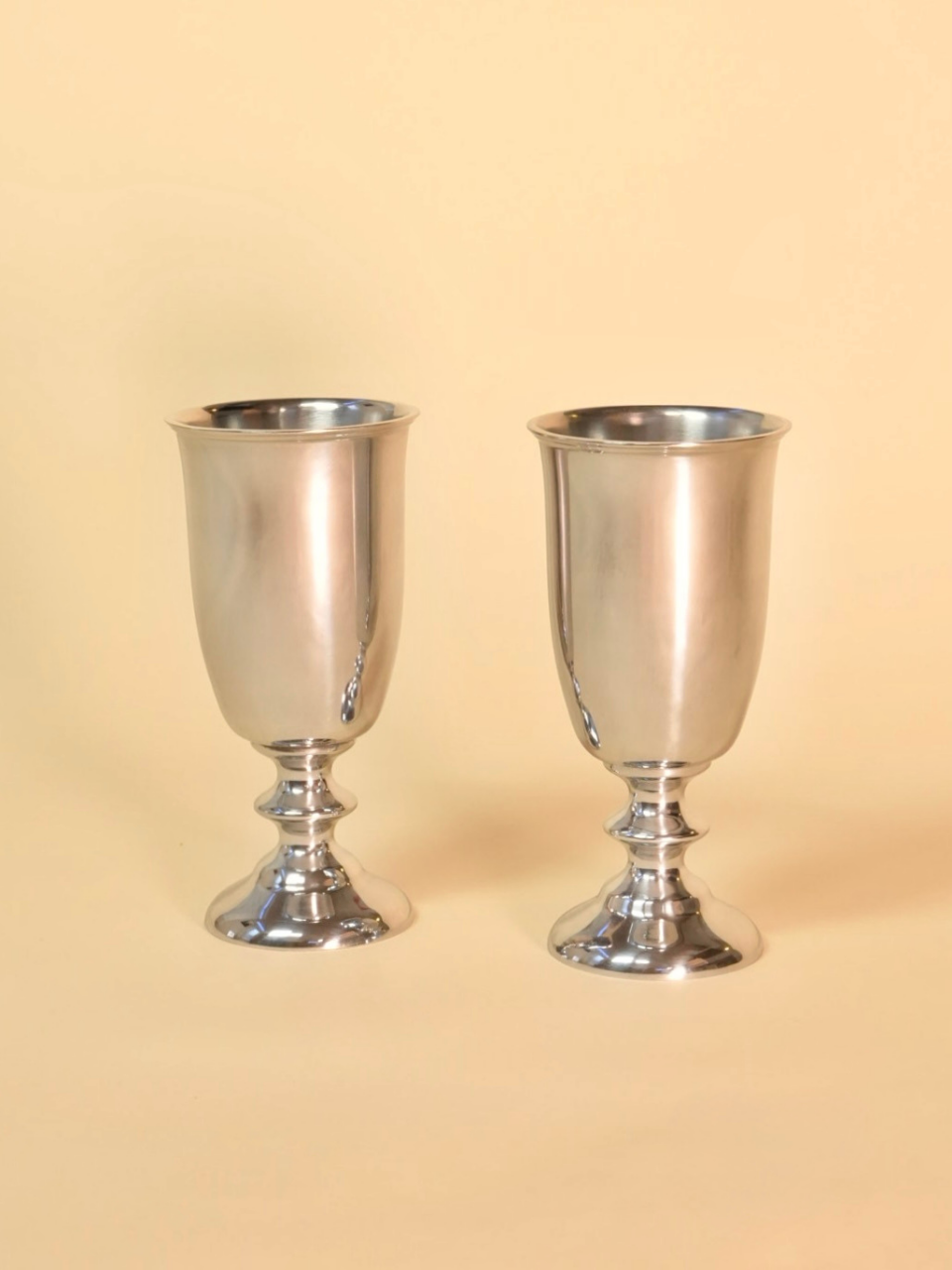 Two silver goblets on a beige background