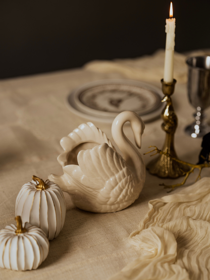Decorative swan figurine on a table with pumpkins and a candle.