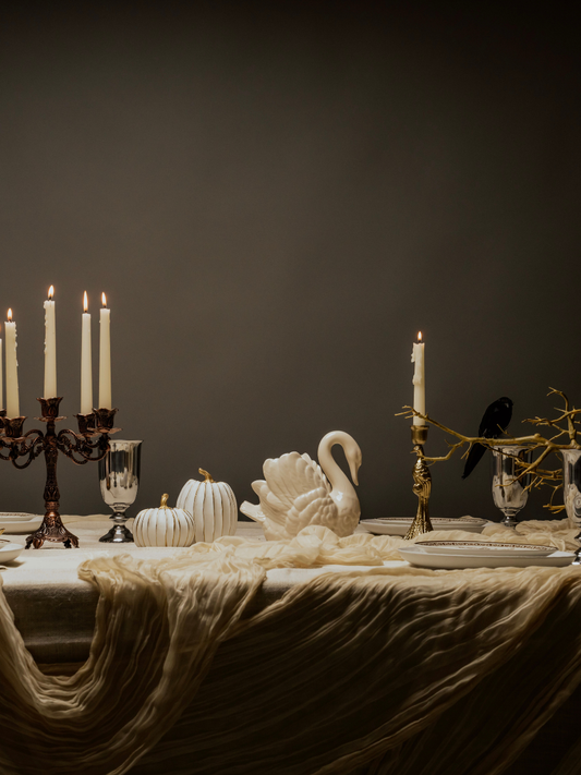 Decorative table setting with candles, swan sculpture, and pumpkins against a dark background