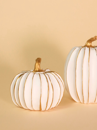 Two white pumpkins with gold accents on a beige background